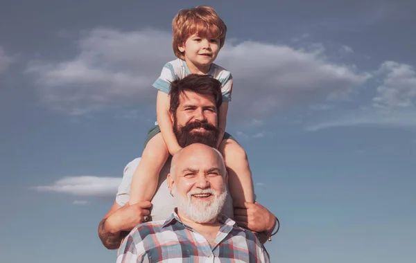 Babalar Günü. Büyükbaba, baba ve oğul kucaklaşıp birlikte eğleniyorlar. Mutlu çocuk yaz gökyüzü arka planında oynuyor. — Stok fotoğraf