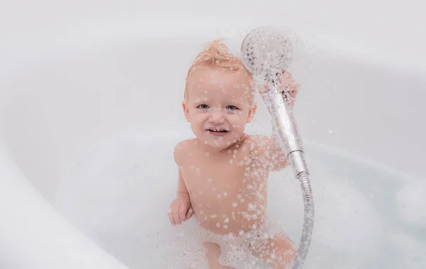 Bébé drôle jouant avec l'eau et la mousse dans un grand évier de cuisine. Petit enfant dans une baignoire . — Photo