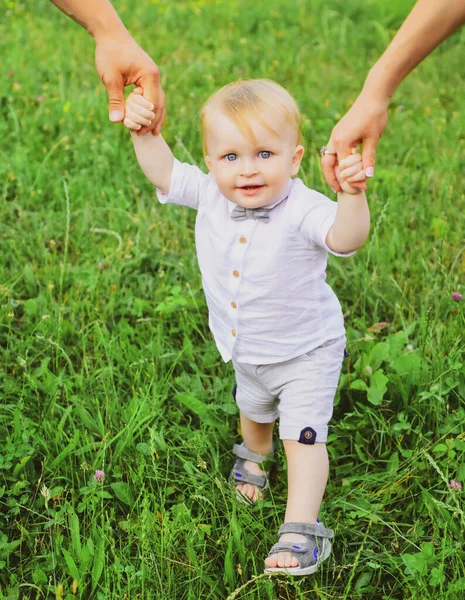 Les parents main et enfant premier pas. Bébé jouant dans l'herbe verte. Enfant s'amusant sur le pique-nique en famille dans le jardin d'été. Portrait d'une jeune famille heureuse enseignant à bébé à marcher dans le parc. — Photo