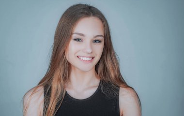 Beyaz arka planda duran tatlı sarışın bir kızın portresi. Uzun saçlı, rahat gömlekli, mutlu bir yüz ifadesiyle kameraya gülümseyen güzel bir kızın yakın portresi..