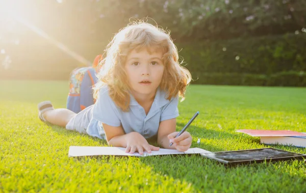 Porträtt av glad pojke med bok skriva anteckningar i copybook i parken. Förskolebarn. Liten unge läser bok i trädgården. — Stockfoto