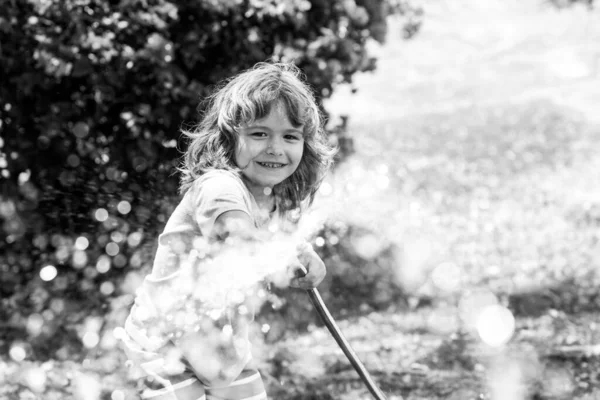 Kind gießt Blumen und Pflanzen im Garten. Kind mit Wasserschlauch im Hinterhof. Kindergärtnerei. Kinder-Sommerspaß im Freien zu Hause. — Stockfoto