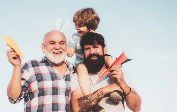 Uçmayı hayal et. Mutlu çocuk dışarıda oynuyor. Mutlu gülümseyen çocuk, baba kameraya bakıyor. Erkek çok nesilli aile.