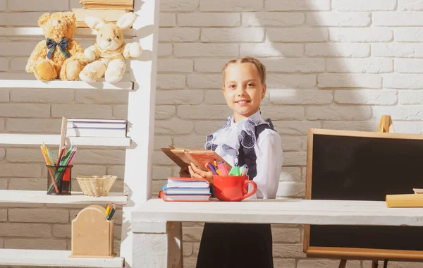 Okul üniforması giyen ve egzersiz kitabı tutan gülümseyen öğrenci kız. Okuldaki ilk günüm. Şirin küçük çocuk ders çalışıyor..