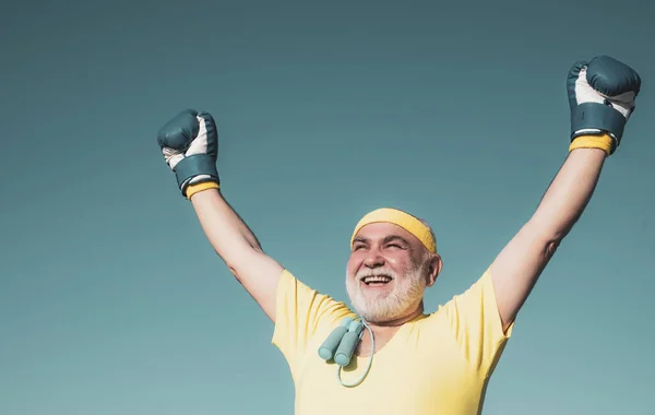 권투 글러브를 쓴 행복 한 어르신이시네요. 파란 하늘 배경 위에 나이든 권투 선수의 초상화. 건강 한 늙은이 권투 글러브. — 스톡 사진