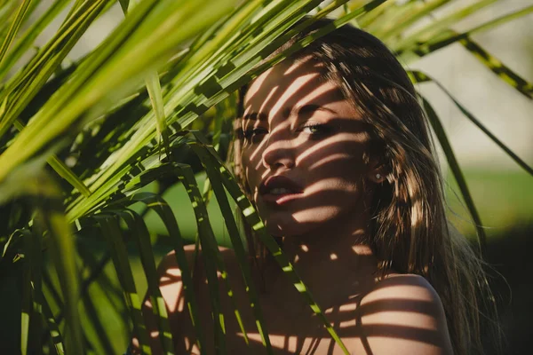 Portret młodej kobiety za liśćmi palmy. Egzotyczne liście tropikalne w pobliżu jej twarzy. Piękno, moda, kosmetologia, przyroda i letnie spa. — Zdjęcie stockowe