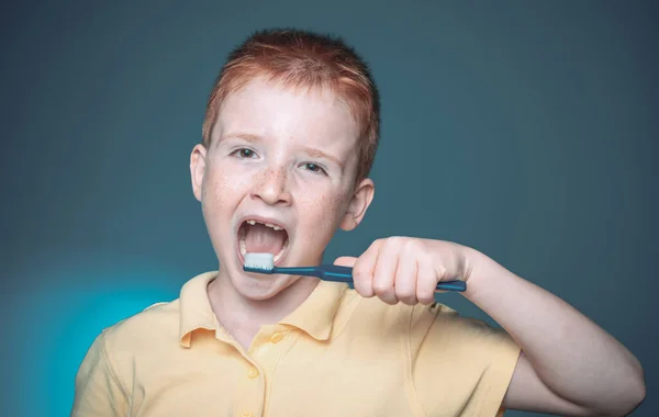 Мальчик чистит зубы. Счастливый маленький мальчик чистит зубы. Улыбающийся мальчик без одного зуба с зубной щеткой изолирован на синем фоне. Дизайн рубашки, здоровье, гигиена полости рта. — стоковое фото