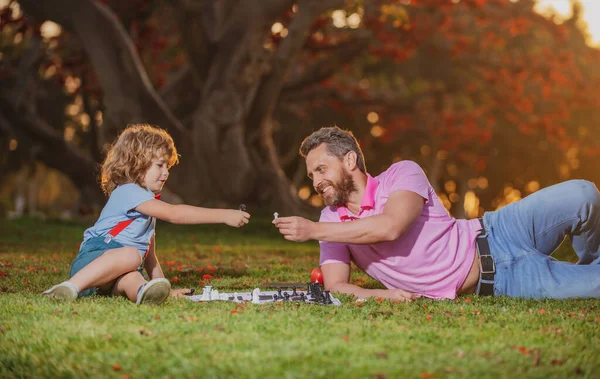 Syn ležel na trávě a hrál šachy s otcem. Inteligentní dítě, chytré děti. — Stock fotografie