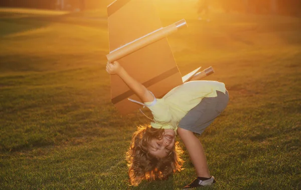 Caucasian kid playing with toy plane on sunny golden sunset sky background outside on grassy summer hill. Dreaming about happy future concept. Expression kids face. — Foto de Stock