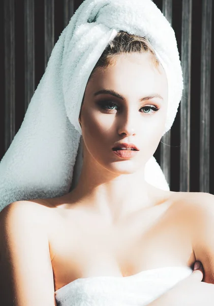 Portrait of sensual woman with a towel wrapped around her head looking at camera. Beautiful lady drying her hair with white towel after shower. — Photo