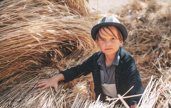 村の秋の休日にかわいい男の子。少年は秋に子供服を宣伝する。干し草の中で頭に帽子をかぶった楽しい男。幸せな子供時代. — ストック写真
