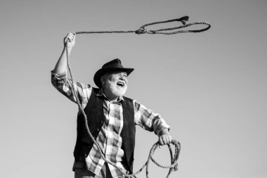 İple vahşi batı kovboyu. Sakallı batılı adam kahverengi ceketli ve şapkalı kement atıyor. At ya da inek yakalıyor..