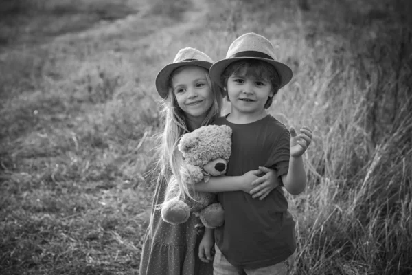 Barn som har kul i fält mot naturen bakgrund. Glada barn flicka och pojke kram på äng på sommaren i naturen. Underbara barn. Alla hjärtans dag kort. — Stockfoto