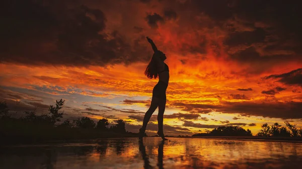 Silhouette nera di bella ragazza o bella donna, sexy modello sottile, con i capelli lunghi posa sulla spiaggia al tramonto all'aperto su sfondo cielo viola — Foto Stock