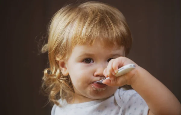 Baby eet met vies gezicht. Vrolijk lachend kind eet zichzelf op met een lepel Baby eet met vies gezicht. Glimlachend kind dat eten eet in de keuken. Jongen hongerig. — Stockfoto