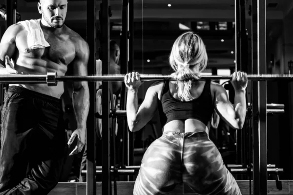 Coppia sexy sportiva con bilanciere in palestra. Coppia sportiva in palestra. Personal trainer aiutare la donna a fare esercizio. — Foto Stock