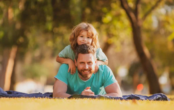 Padre e hijo tendidos en la hierba. La gente se divierte al aire libre. Concepto de vacaciones felices y familia amigable. — Foto de Stock