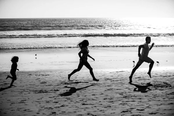 日の出の海のビーチに沿って家族のジョギングのシルエット。アウトドアワークアウト、ランナーのシルエット、スポーツや健康的な家族のライフスタイル. — ストック写真