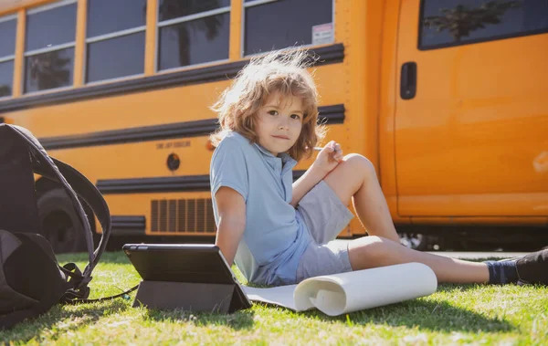 Schüler erledigt Hausaufgaben auf Rasen im Park neben dem Schulbus. Schulkind im Freien. — Stockfoto