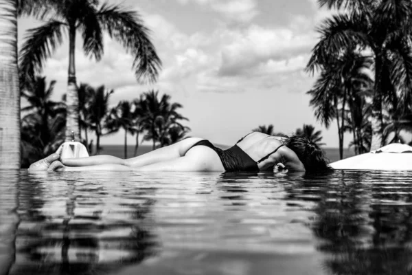 야자수와 푸른 하늘로 수영장을 헤엄치는 섹시 한 소녀. 수영장에서 일광욕하는 여자. — 스톡 사진