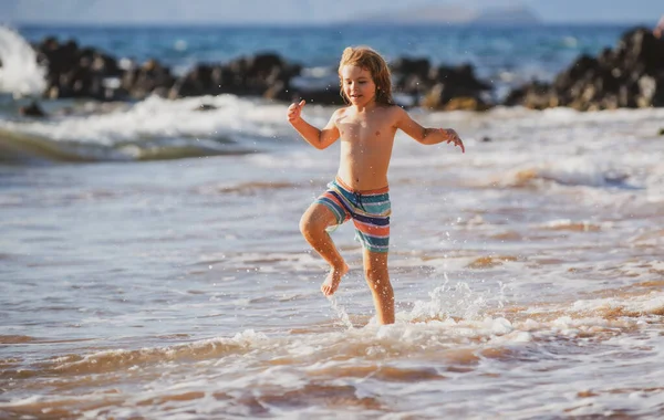 休暇中の夏の日に海の波の中で活発な小さな男の子が飛び散っています。子供と家族の休日の概念. — ストック写真