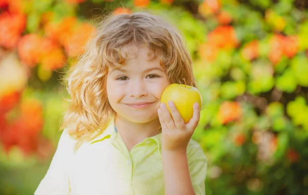 Портрет маленького мальчика, держащего и поедающего яблоко на зеленом фоне природы. — стоковое фото
