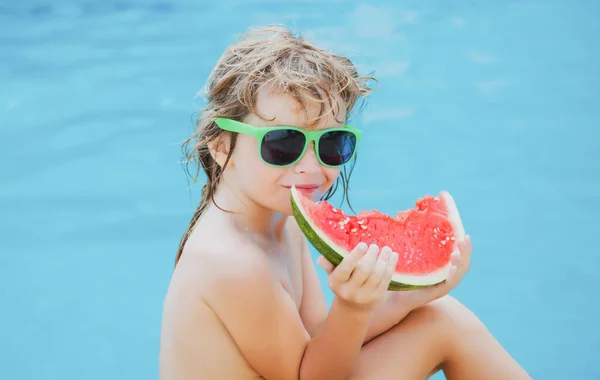 Bambino ragazzo mangiare anguria sulla piscina in occhiali da sole. Faccia divertente per bambini. — Foto Stock