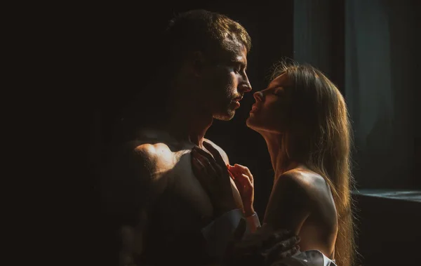 Een man die een sensuele vrouw omarmt en gaat kussen. Liefdevol koppel zoenen in de slaapkamer over zwarte achtergrond. Echte liefde op Valentijnsdag. — Stockfoto