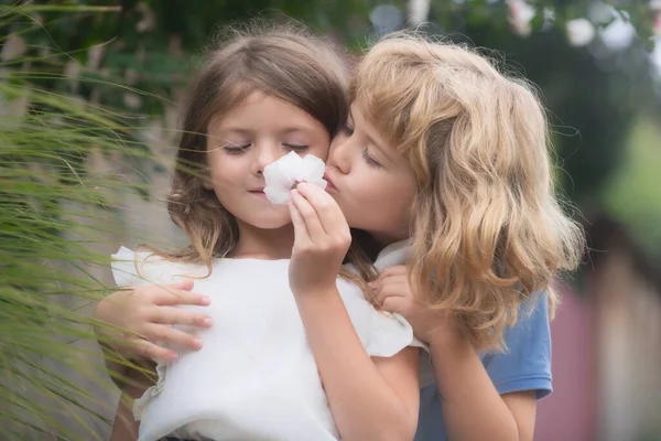 Twee kleine kinderen knuffelen en kussen elkaar in de zomertuin. Kinderen zijn verliefd. Romantische jongen en verlegen meisje, het geven van een bloem voor liefde en romantiek. — Stockfoto