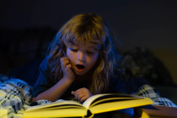 A little cute boy reading a book lying on the bed. Child reading a book on bedtime night. Happy childhood, dreaming child. —  Fotos de Stock