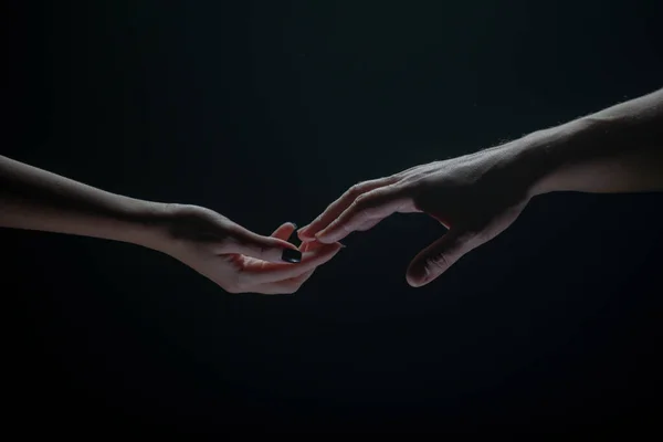 Twee handen strekken elkaar uit, zwarte achtergrond. Verliefd stel met hads, close up. Helpende hand, steun, vriendschap. — Stockfoto
