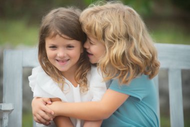 Child boy and girl hugging each other with love in the spring garden. Two little kids hugging in the park. Kids friends playing together outdoor. Happy children having fun outdoors. Shy girl.