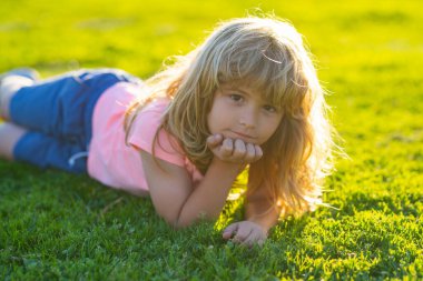 Spring child face. Smiling child boy with grass background. Happy child lying on green grass. Smiling boy having fun outdoor in garden.