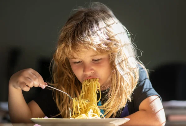 Close up portrait of funny kid eating noodles pasta spaghetti. Little boy having breakfast in the kitchen. — Stok fotoğraf