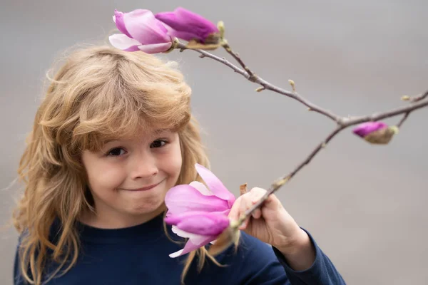 Όμορφο ξανθό μικρό παιδί με μακριά μαλλιά μυρίζει λουλούδι. Ανοιξιάτικο παιδικό πρόσωπο. Αστείο πρόσωπο για παιδιά. Χαρούμενο ξανθό παιδί με λουλούδια. Το παιδί ονειρεύεται και χαμογελά στο ανοιξιάτικο χωράφι. — Φωτογραφία Αρχείου