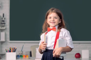 Sınıfta üniformalı, gülümseyen güzel bir kızın portresi. Dahi çocuk, bilgi günü.