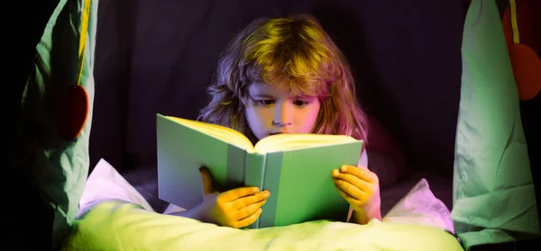 Child reading a book in the dark home. Close up portrait of Boy sitting on in living room watching pictures in story book. Kid doing homework for elementary school. Children study. — Stock Photo, Image