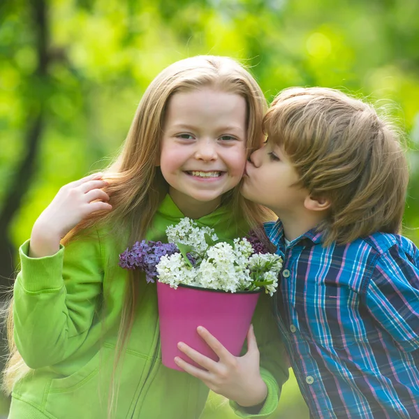 Duas crianças pequenas abraçam-se e beijam-se no jardim de verão. Os miúdos apaixonam-se. Amizade e infância. Menina beijando menino pequeno ao ar livre no parque. — Fotografia de Stock