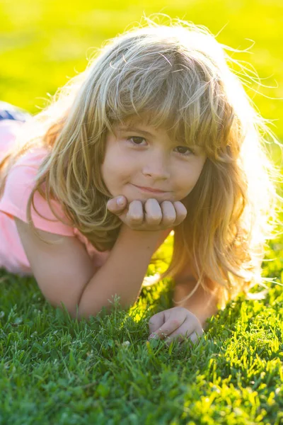 Sommarbarns ansikte. Leende pojke med gräs bakgrund. Sommar barn utomhus porträtt. Glada barn njuter på gräsplan och drömmer. Barn på grönt gräs bakgrund. — Stockfoto
