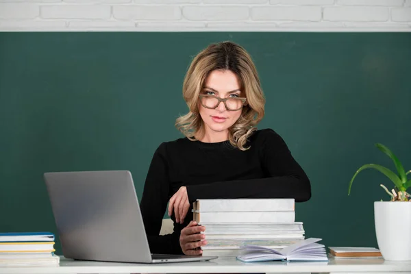 Sensual student woman in eyeglasses near blackboard. Sexy girl sit on table on chalkboard. — Stockfoto