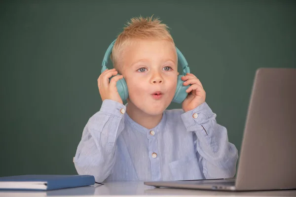 Chytrý chlapec ve sluchátkách sedí za stolem, studuje on-line na notebooku ve škole, klever dítě nosí sluchátka v notebooku učení pomocí internetových lekcí. První den ve škole. — Stock fotografie