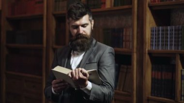 Klasik kütüphane dolabında kitap okuyan konsantre bir adam. Ev kütüphanesi. İş adamı klasik bir iç mekanda oturuyor, elinde kitap tutuyor. Dolabında takım elbiseli bir iş adamı. Sakin yüzlü olgun bir adam eğleniyor.