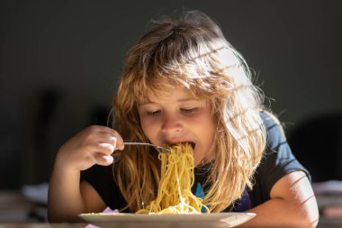 Küçük çocuk mutfakta spagetti yiyor. Bulanık arka planda yemek yiyen çocuk. Aç küçük çocuk yemek yiyor. Çocuklar için ev yemeği.