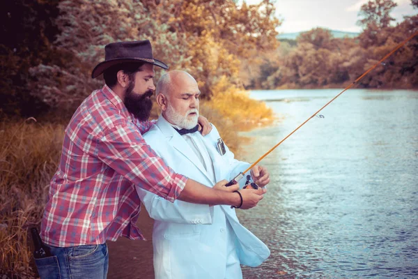 Two men friends fishing. Flyfishing angler makes cast, standing in river water. Old and young fisherman. — стоковое фото