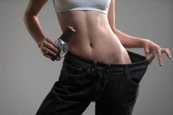 Cintura fina. Mulher magro em jeans oversize, conceito de perda de peso. Alimentos dietéticos, dieta de chocolate. — Fotografia de Stock