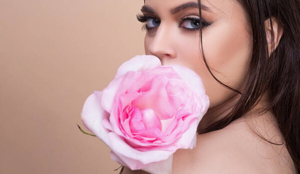 Fashion portrait of young beautiful woman with blue eyes and pink rose. Close-up portrait of a beautiful young girl with a pink rose near face.