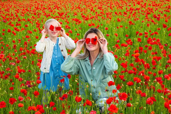 Mom with a child girl in a field of red poppies enjoys nature. Mother and little daughter in the poppy field. A young woman with her daughter in in a poppy field. Happy motherhood. — стоковое фото