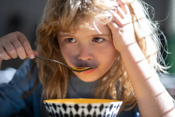 Unhappy sad child boy with spoon eats itself. Kid eating food on kitchen. — Stockfoto