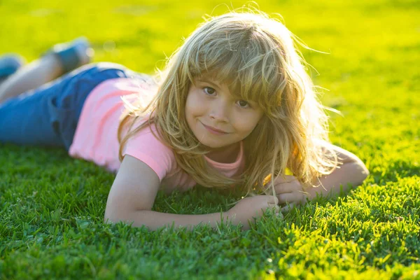 Cara infantil de primavera. Niño sonriente con fondo de hierba. Feliz niñito tirado en la hierba en el día de primavera. Retrato de un niño sonriente acostado sobre hierba verde en el parque. — Foto de Stock