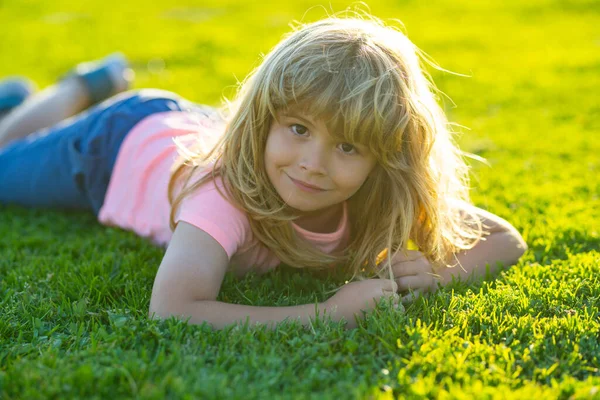 Spring child face. Smiling child boy with grass background. Happy little boy lying on the grass at the spring day. Portrait of a smiling child lying on green grass in park. — Stock Fotó